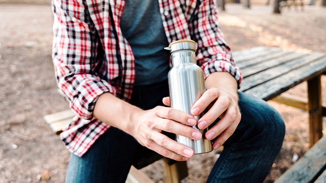 person holding a reusable sustainable water bottle in a park